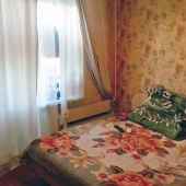В спальной комнате стоит кровать и стенка мебельная у стены напротив